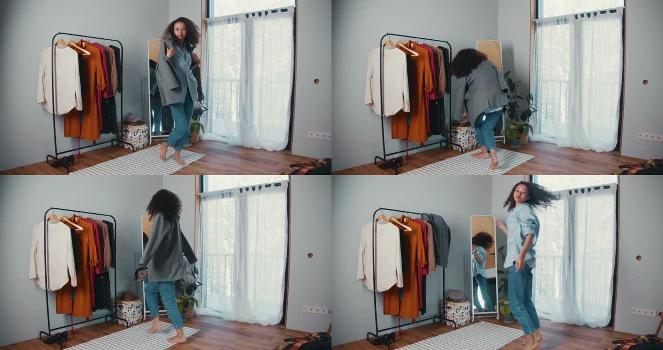 快乐美丽的年轻非洲裔美国妇女，卷发跳舞，在舒适的大衣柜里摆姿势试穿衣服