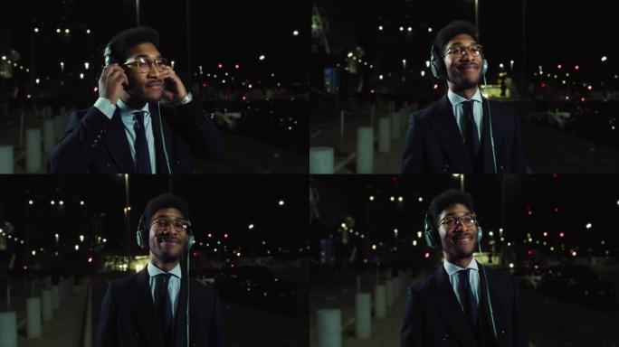 一个英俊时尚的黑人男性晚上在街上行走并戴上耳机的特写镜头。工作一天后享受音乐的员工。一个男人用优美的