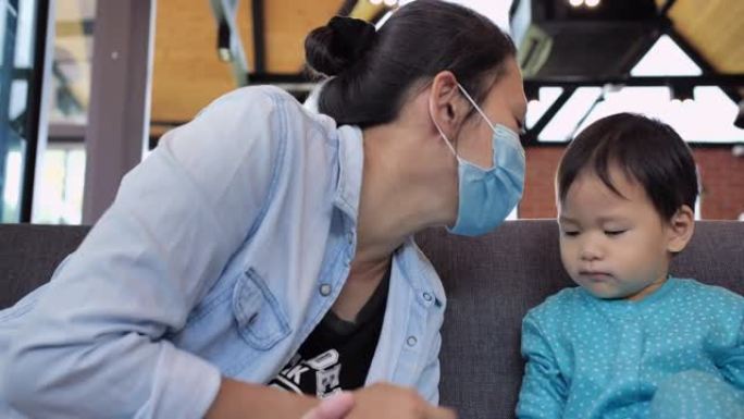 亚洲年轻母亲家庭与12个月大的男婴儿子戴医用口罩表示喜欢亲吻面部预防冠状病毒流行或Covid-19.