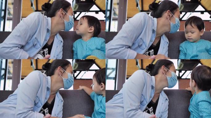 亚洲年轻母亲家庭与12个月大的男婴儿子戴医用口罩表示喜欢亲吻面部预防冠状病毒流行或Covid-19.