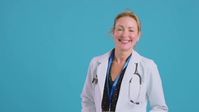 微笑的女医生穿着白色外套站在蓝色工作室背景前的肖像