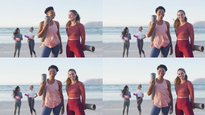 一群不同的女性朋友在海滩上拿着瑜伽垫