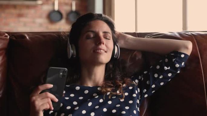放松的年轻西班牙裔白人妇女戴着耳机听音乐。