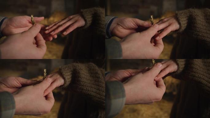 年轻男性农夫的电影宏观镜头在与他心爱的牛棚女人求婚后，将一枚干草制成的戒指戴在新娘未来妻子的手指上。