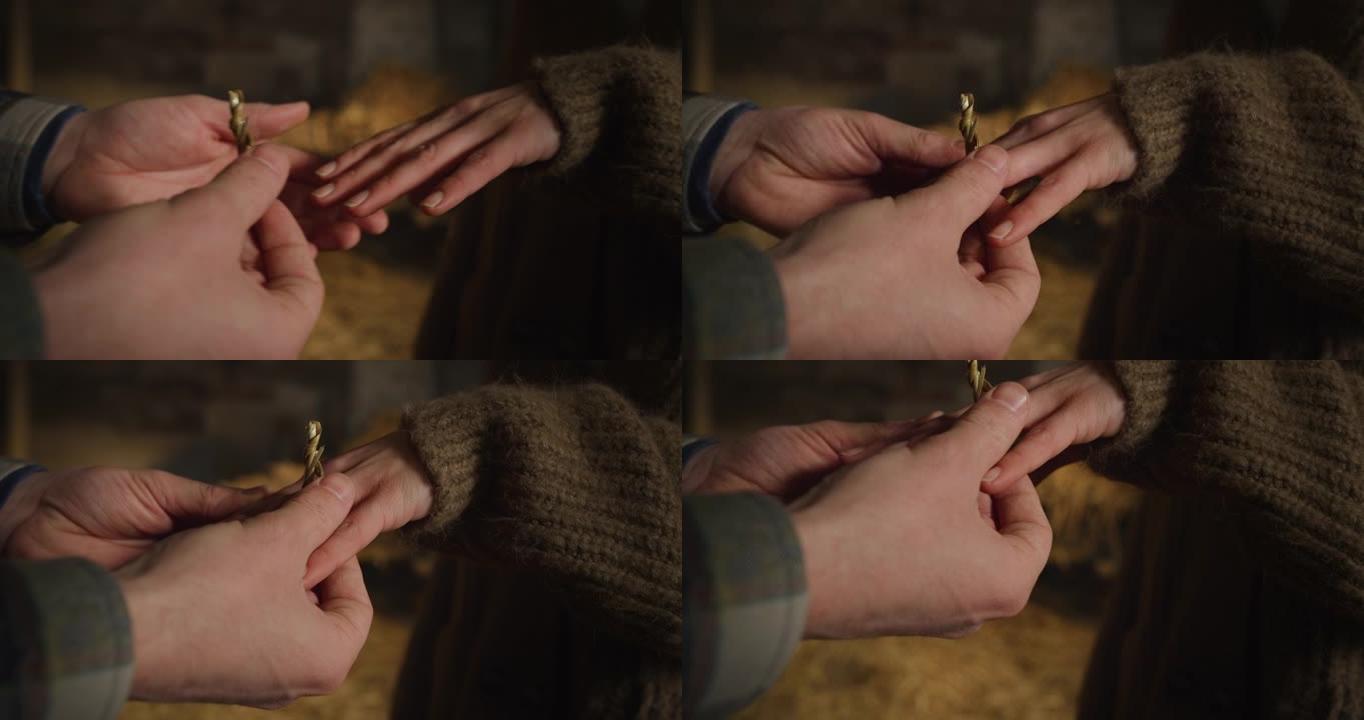 年轻男性农夫的电影宏观镜头在与他心爱的牛棚女人求婚后，将一枚干草制成的戒指戴在新娘未来妻子的手指上。