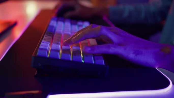 特写镜头亚洲盖伊游戏玩家使用键盘和鼠标控制器在家里的办公桌上玩霓虹灯电脑视频游戏。
