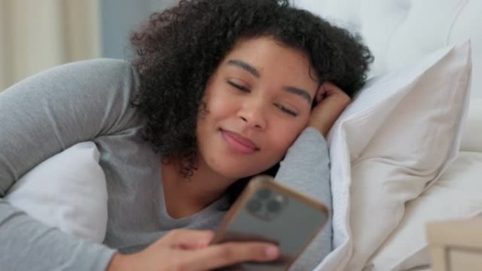 黑人妇女躺在床上，在社交媒体应用程序或互联网交流上开心的电话聊天。智能手机打字女孩，卧室微笑与网络技