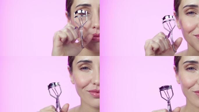 4k视频片段，一个迷人的年轻女子在粉红色的工作室背景下使用睫毛夹