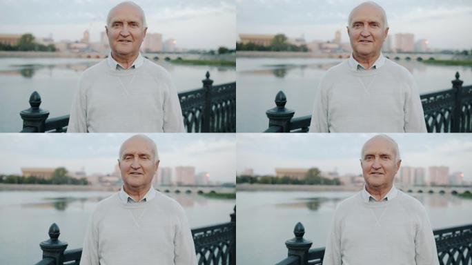 健康的老人站在河堤户外，满意地看着相机