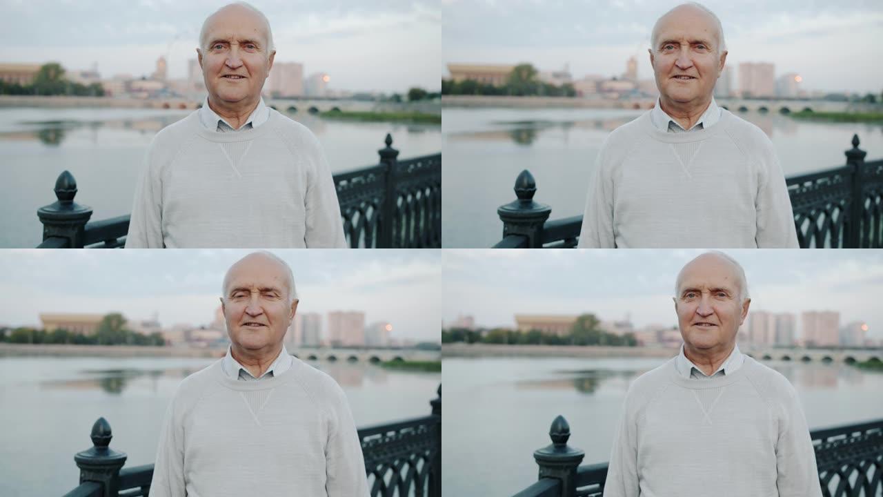 健康的老人站在河堤户外，满意地看着相机