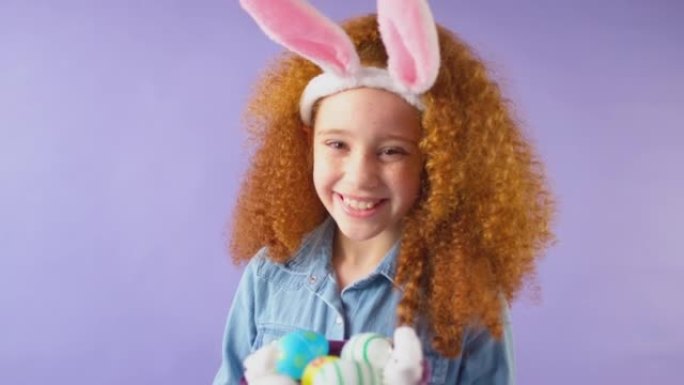 工作室拍摄的女孩戴着兔子耳朵，拿着一篮子紫色背景下的复活节彩蛋-慢动作拍摄