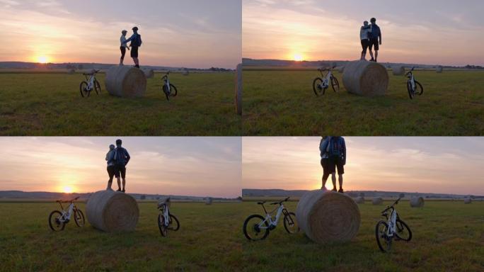 SLO MO爱着一对骑自行车的人站在草捆上享受日落