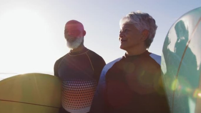 老年非裔美国夫妇在海滩上与冲浪板一起散步