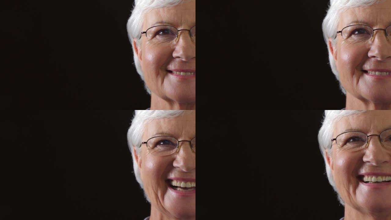 一个快乐的高级女人的半脸孤立在黑暗的背景上，有复制空间。一位老人，退休女性戴着眼镜，笑容灿烂。退休的