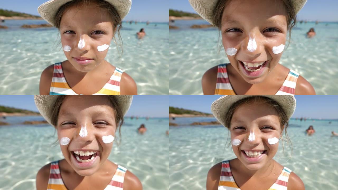 一个小女孩脸上带着防晒霜的有趣肖像看着相机，在海滩上的水中笑着。暑假玩得很开心的女孩子用广角镜头拍摄