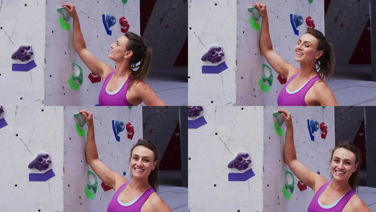 微笑的白人妇女在室内攀岩墙上抓住攀岩墙的肖像