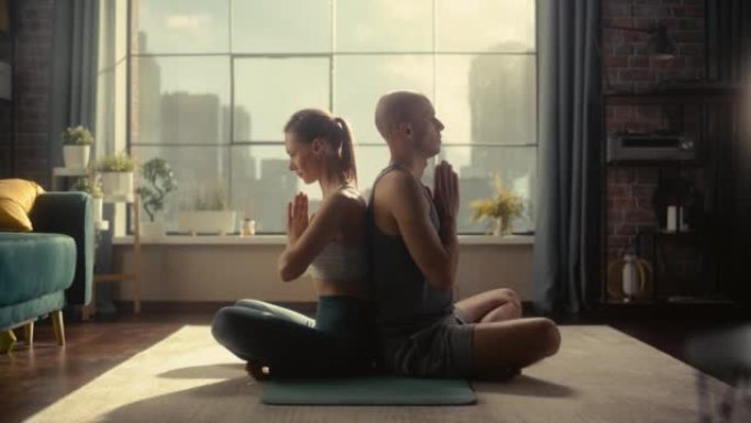 年轻美丽的夫妇锻炼身体，早上在阳光明媚的阁楼公寓练习冥想。健康的生活方式、健身、幸福和正念概念。