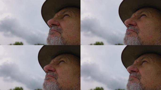 气候变化。一位戴着帽子的老农民的特写肖像看着天空等待下雨以缓解干旱