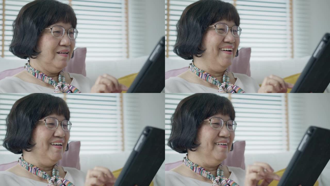坦率的亚洲老退休女士使用平板电脑在网上或金融支付转账，并以快乐和积极的态度阅读文字，微笑或大笑。具有