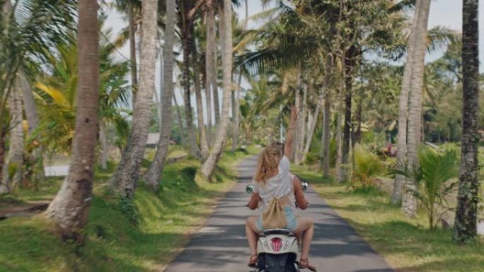 热带岛屿上骑摩托车的旅行情侣快乐的女人举起双臂庆祝自由享受与男友骑摩托车旅行的假期公路旅行