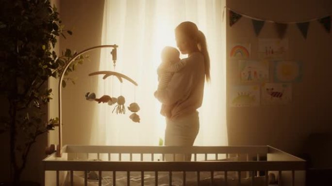 快乐母亲在舒适温暖的儿童卧室里抱着一个可爱的新生婴儿的真实镜头。有爱心的妈妈和幼儿在家里结为纽带。童