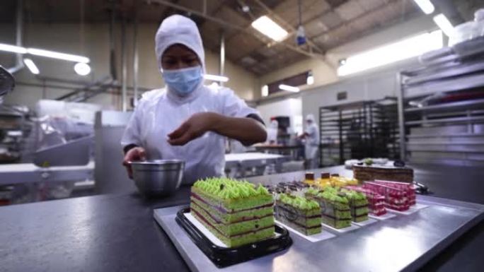 拉丁美洲妇女在一家工业面包店用开心果装饰美味的蛋糕