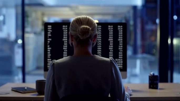 程序员或网络安全员工在办公室加班的后视图。熟练的女性网络专家晚上在工作场所在计算机上编写后端算法