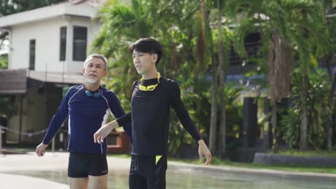 亚洲华裔高级男子和他的儿子在游泳课前在泳池边热身