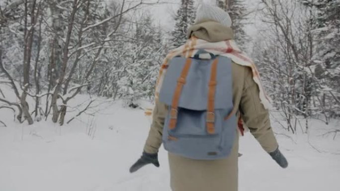 快乐的年轻人的慢动作，背包在雪树间的冬季树林中行走