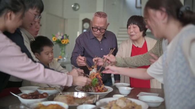 亚洲华人mutli世代家庭在团圆饭中与传统美食Lou sang (生鱼菜) 庆祝除夕