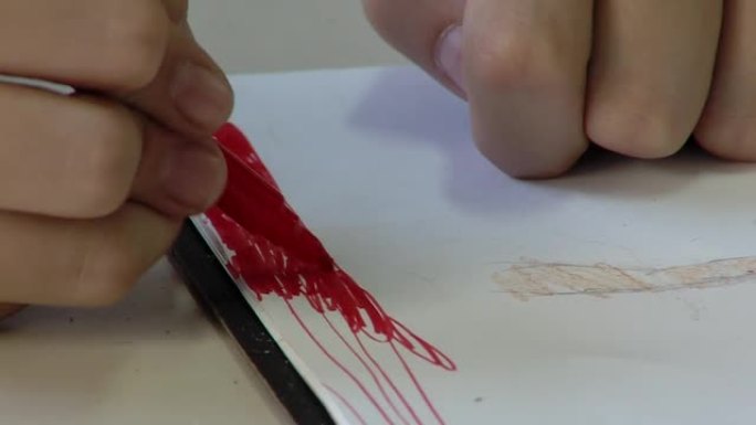 小学生坐在美术课上用红色记号笔在白纸上素描。特写。