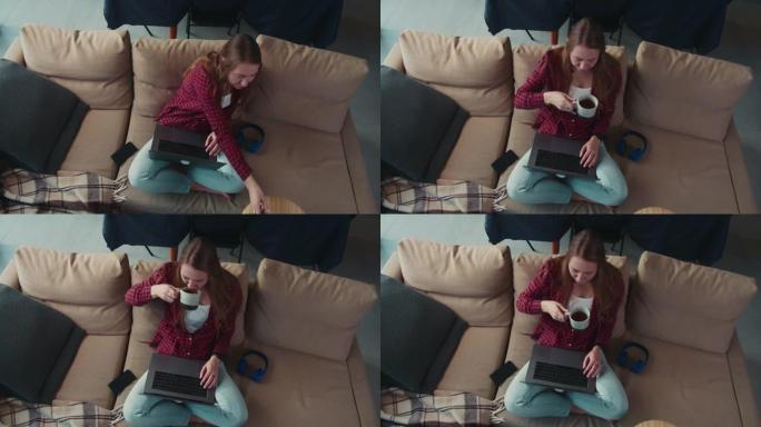 顶视图年轻美丽专注的高加索自由网络开发者女人使用笔记本电脑，在家喝咖啡。