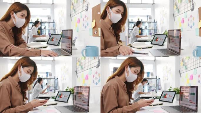 亚洲女商人企业家戴着口罩，在新的正常情况下保持社交距离，以预防病毒，同时在办公室使用笔记本电脑和电话