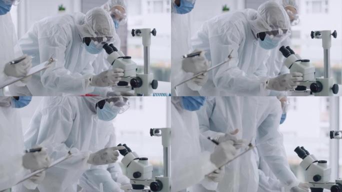 穿着危险品套装的科学家在实验室里使用显微镜。一组微生物学家的特写镜头，讨论法医研究，同时分析医学样本
