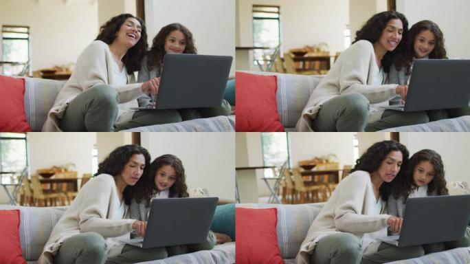 快乐的混血母女坐在沙发上，玩得开心，用笔记本电脑