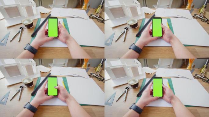 建筑师坐在办公室的办公桌上的POV镜头，使用带有绿色屏幕的手机进行计划-慢动作拍摄