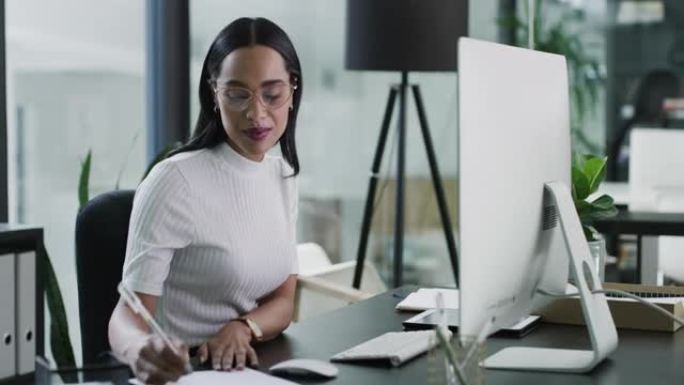 一位年轻的女商人在现代办公室中使用计算机并在笔记本中书写的4k视频片段