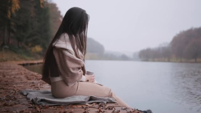 年轻女子坐在湖边的木板路上拿着纸杯