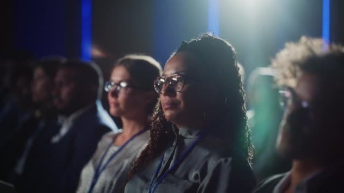在一次科技会议上，一位美丽的黑人女性坐在黑暗拥挤的礼堂里。非洲妇女正在听鼓舞人心的主题演讲。对新技术