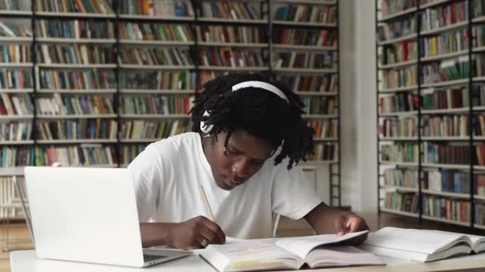 勤奋的非洲男性在耳机中学习图书馆的论文文献
