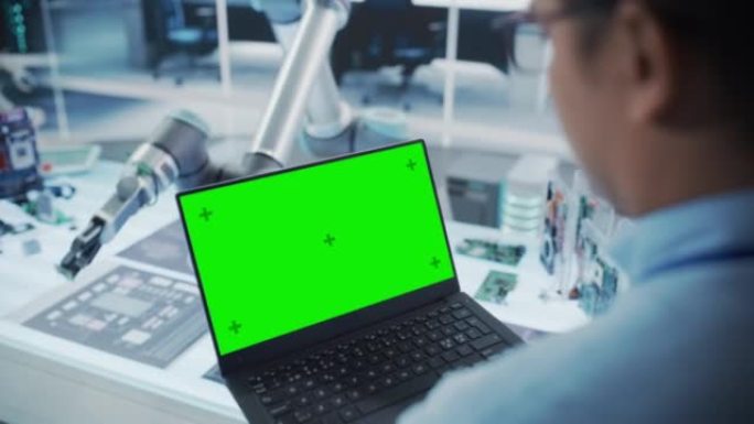 机器人工程师使用带有绿屏模拟显示屏的笔记本电脑拍摄的肩膀。装有微芯片的机械臂。自动化创业研发办公室。