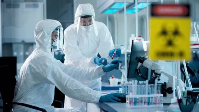 医学实验室: 微生物科学家的多元化团队穿着无菌工作服，口罩交谈，使用计算机分析试管血液样本以治愈冠状