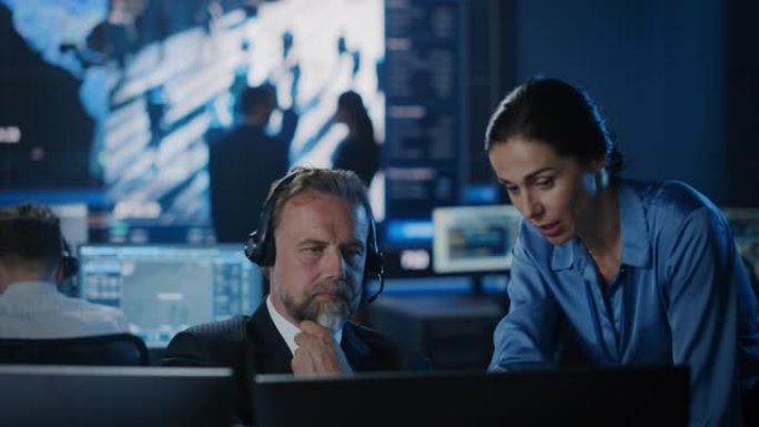 男女政府官员在计算机和大数字屏幕旁边讨论工作事项，并带有带有面部识别软件的卫星监视录像。警方调查人员