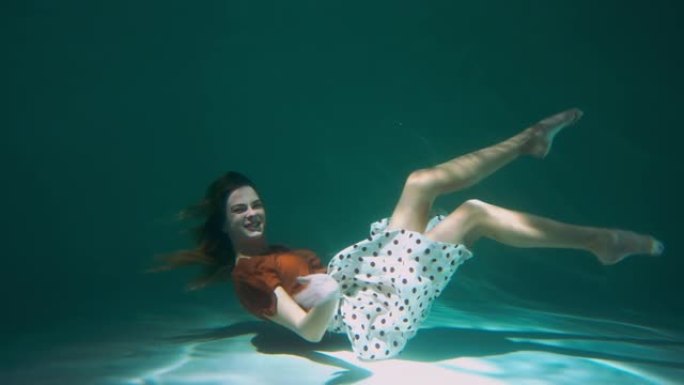 侧视图快乐有趣年轻美丽优雅的舞者女人向前躺着在水下微笑慢动作。