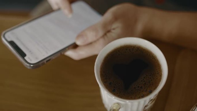 CU在一杯咖啡旁边使用智能手机，泡沫泡沫呈心形