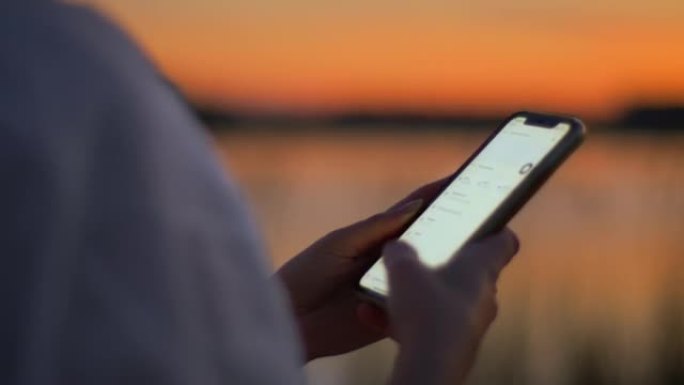 黄昏时，年轻女子在湖边散步时使用手机