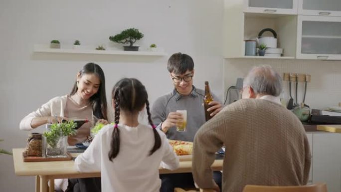 宽镜头: 快乐的亚洲家庭一起享用早餐。开朗的父母，祖父和可爱的女儿一起在家里的餐桌上享用早餐。精彩时