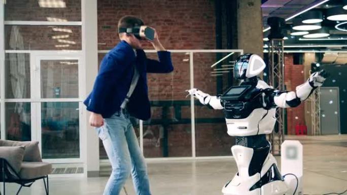 一个戴着VR眼镜的男人正在和机器人跳舞。人工智能、机器人创新、机器人概念。