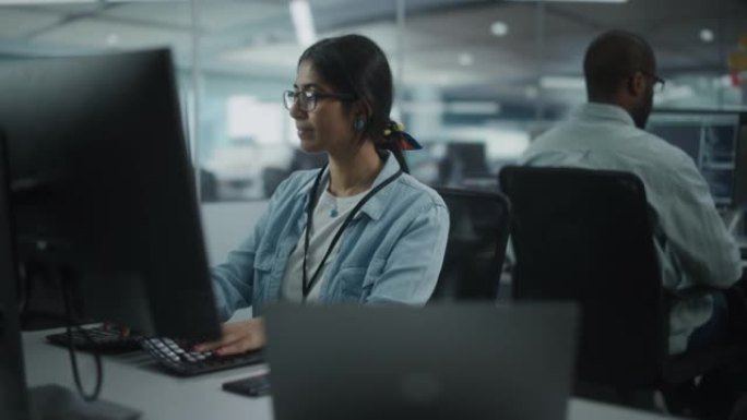 多元化的办公室: 在友好的多民族环境中，才华横溢的印度女孩IT程序员在台式计算机上工作的肖像。戴眼镜