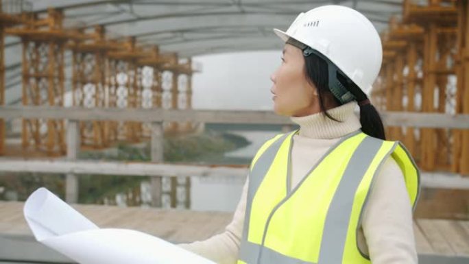 亚洲年轻女服务员在建筑工地学习蓝图的慢动作肖像